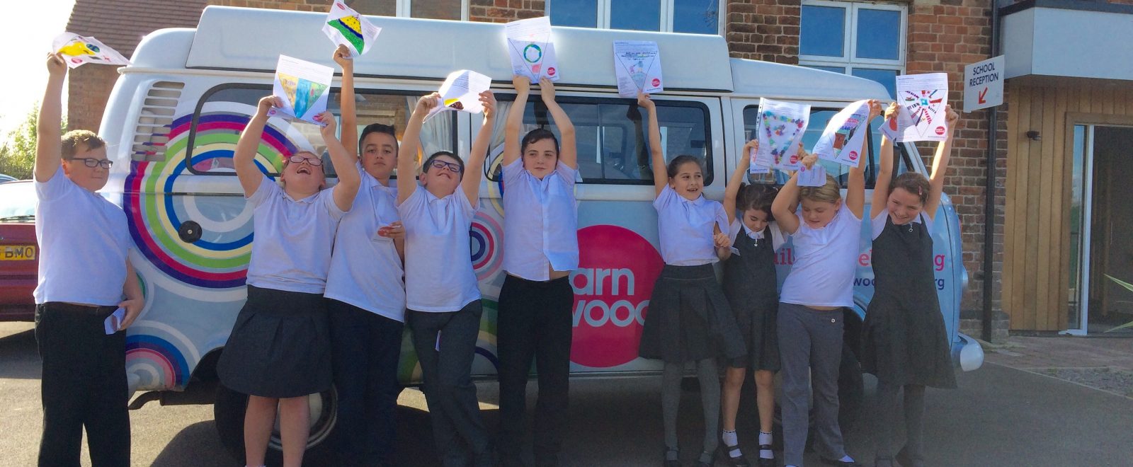 Children holding their drawings in front of the tour camper van.