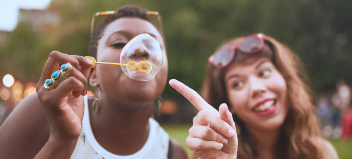 Two multi-cultural friends having fun with soap bubbles in a crowd during an outdoor summer cultural event