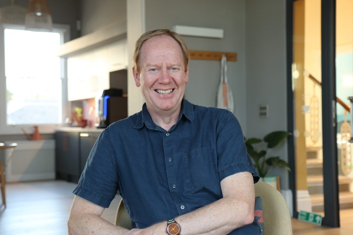 Photo of Ged Cassel, setting in the Barnwood lounge area and smiling