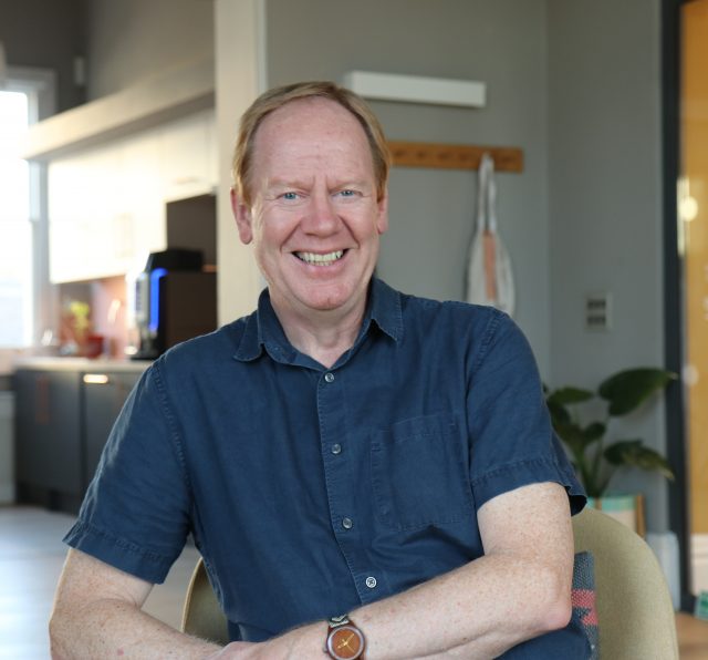 Photo of Ged Cassel, setting in the Barnwood lounge area and smiling