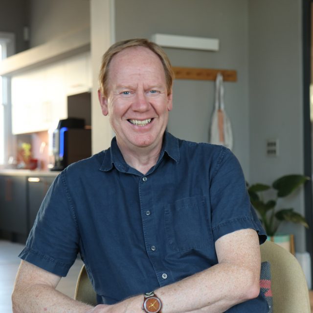 Photo of Ged Cassel, setting in the Barnwood lounge area and smiling