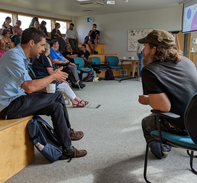 photo shows a room of people at a learning event about Access to Nature, two men are deep in conversation
