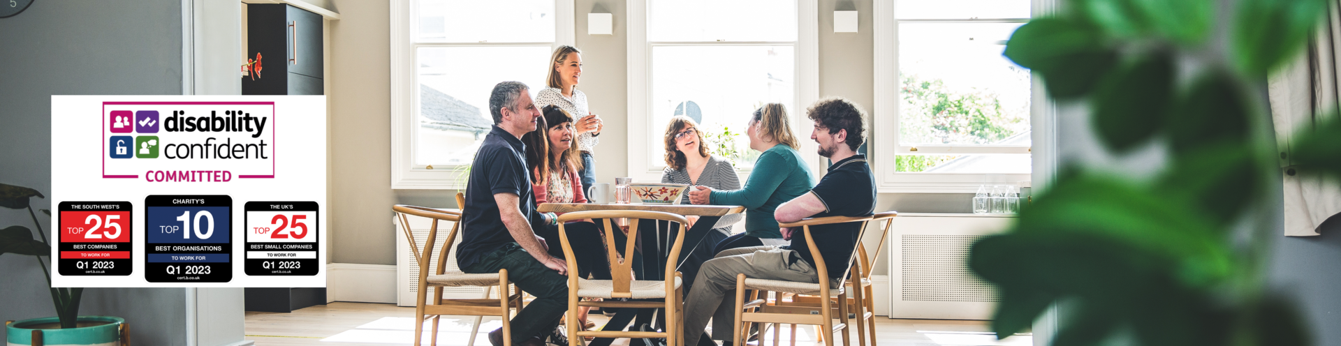 Photograph of Barnwood staff, having lunch in the kitchen on a bright sunny day. There are four logos to the left side, including Disability Confident Committed, The South West Top 25 Best companies to work for, Q1 2023, Charity's Top 10 Best Organisations to work for, Q1 2023 and The UK's Top 25 Best Small Companies to work for, Q1 2023.