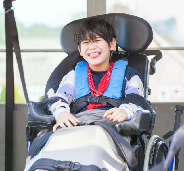 Happy biracial little boy with special needs sitting in wheelchair, riding on yellow school bus lift, going to school