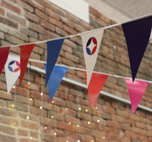 Photo of bunting flags with Barnwood Circle logo and brand colours of pink, purple. orange and blue.