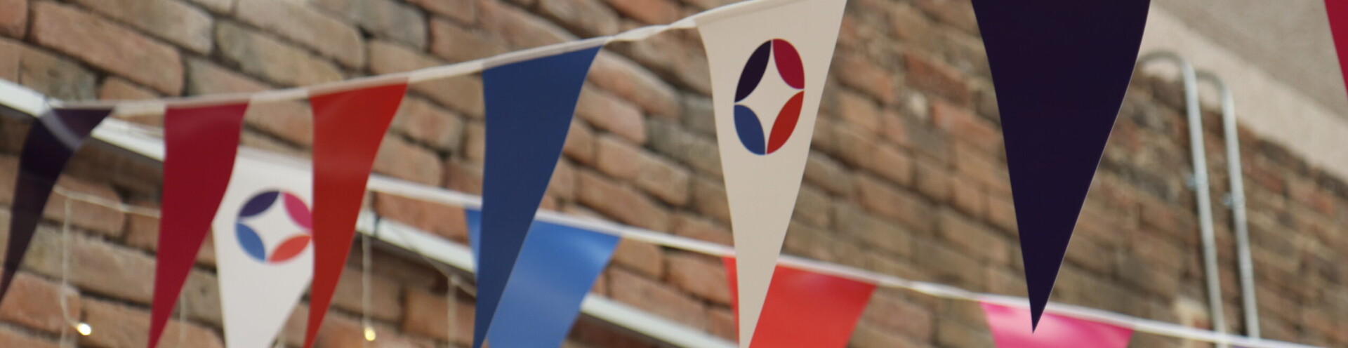 Photo of bunting flags with Barnwood Circle logo and brand colours of pink, purple. orange and blue.