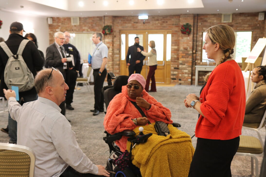 three individuals in a small huddle talking with other huddles of discussion behind them scattered across the room,