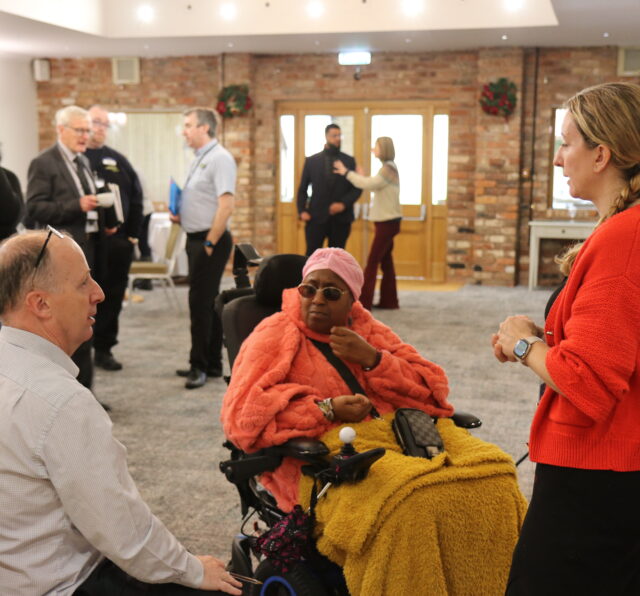 three individuals in a small huddle talking with other huddles of discussion behind them scattered across the room,