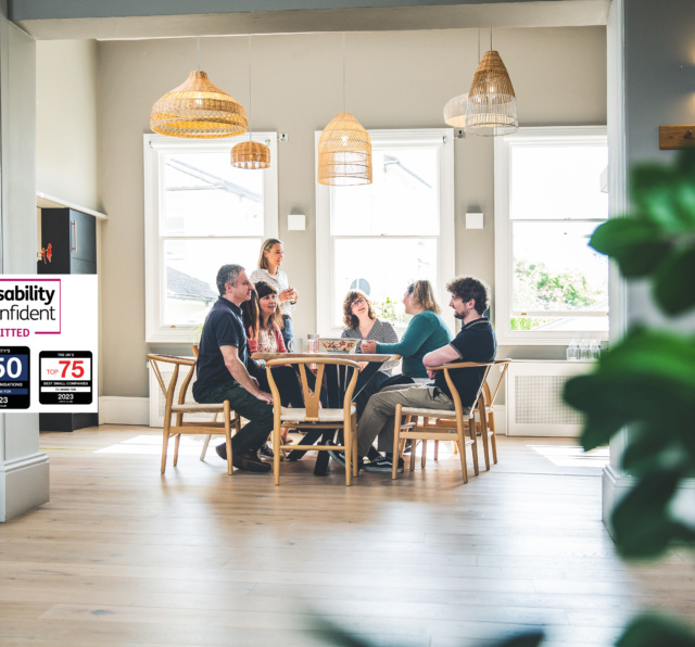 Photograph of Barnwood staff, having lunch in the kitchen on a bright sunny day. There are four logos to the left side, including Disability Confident Committed, The South West Top 25 Best companies to work for, 2023, Charity's Top 10 Best Organisations to work for, 2023 and The UK's Top 25 Best Small Companies to work for, 2023.