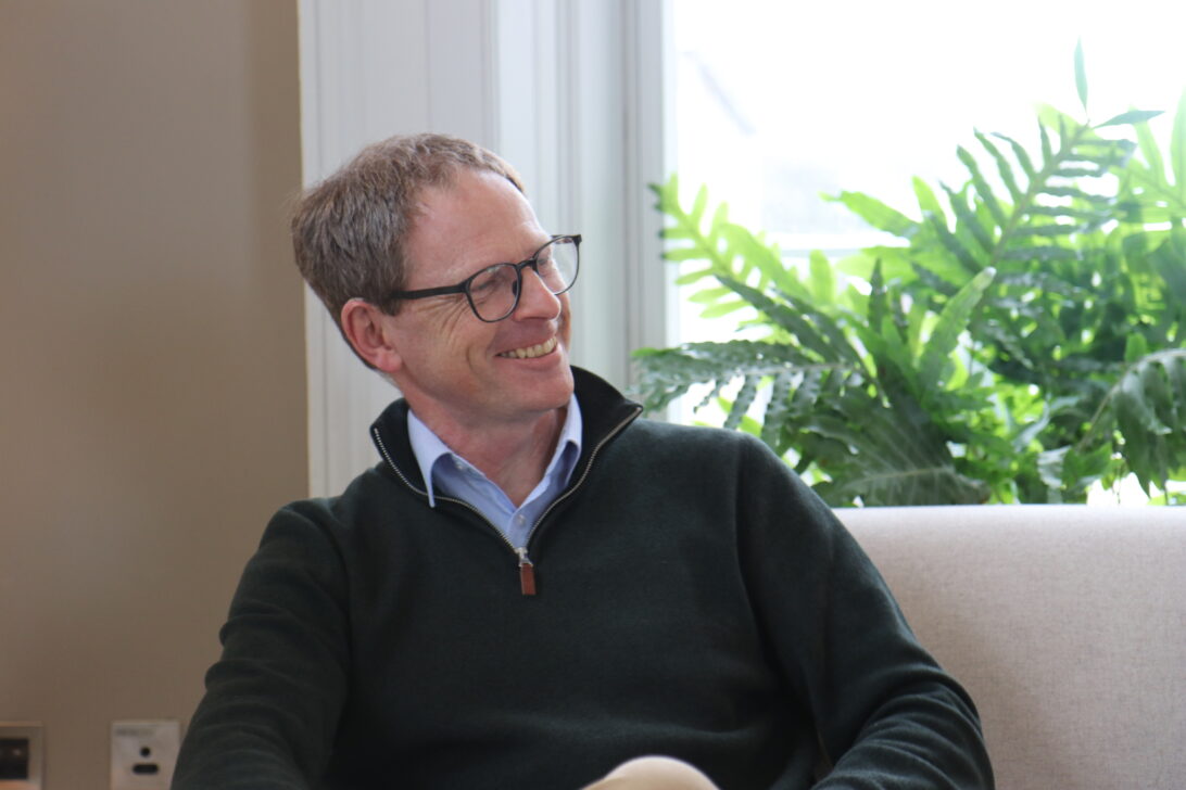 Photo of Graham Reeves, smiling on a sofa.