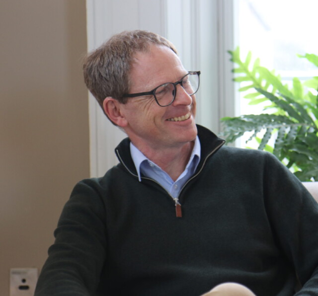 Photo of Graham Reeves, smiling on a sofa.