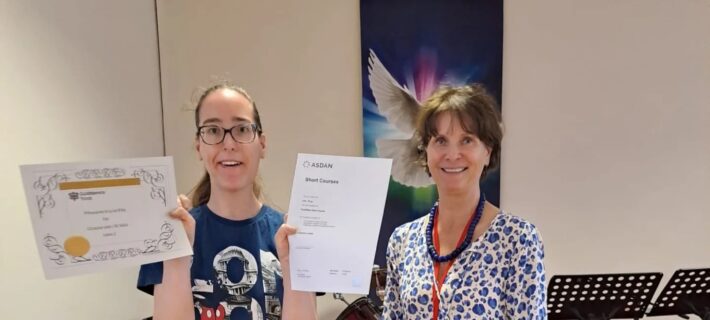A photo of a woman holding up two certificates she has received from the woman standing next to her.