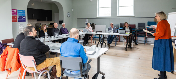 A group of Barnwood staff and Trustees sitting around a table in a meeting listening to someone talking.