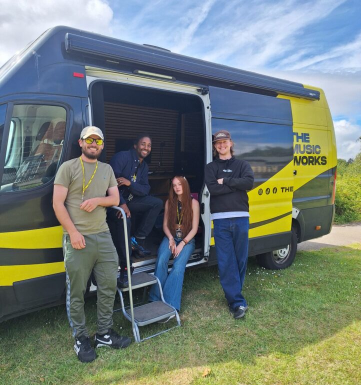 2 people standing next to and 2 people sitting inside the Music Works van.
