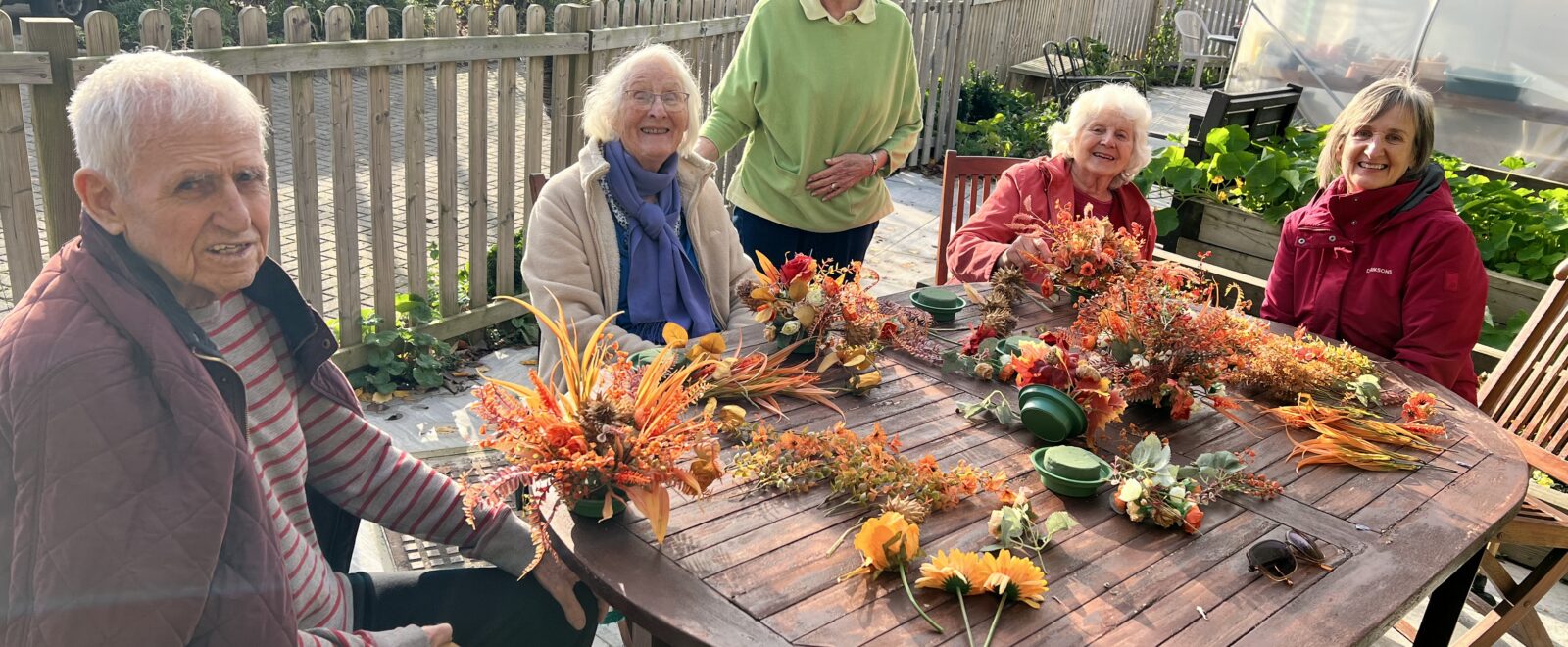 Group of smiling people sitting around a table with plants in front of them.