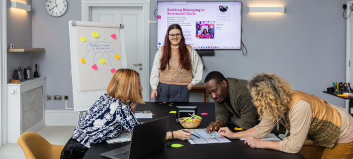 A group of staff members crowding around a table looking at some papers. One person is standing with a flipchart with post it notes on behind them.
