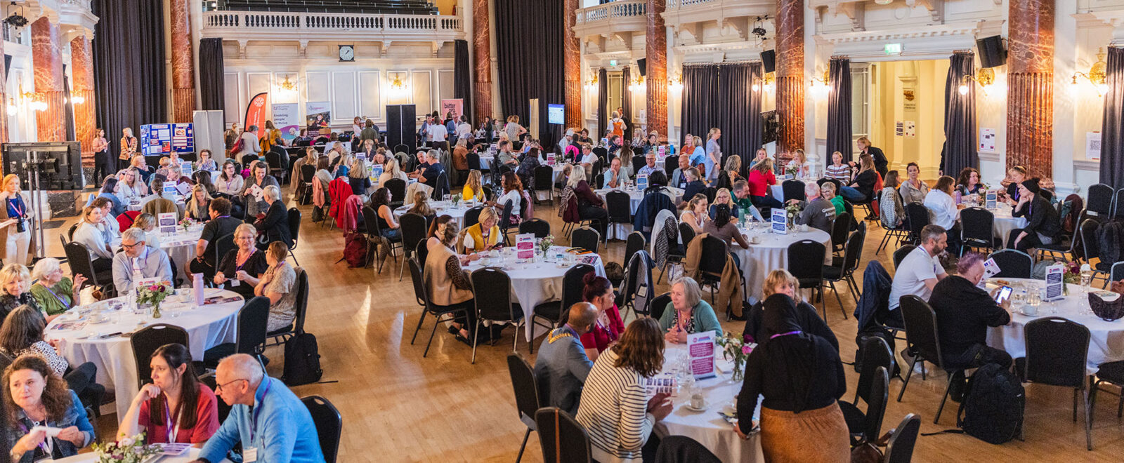 A large room full of tables and people sat around them talking at the funded partner celebration event